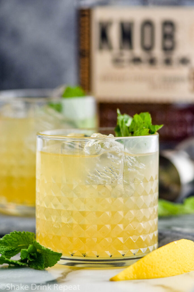 Glass of whiskey smash with ice, whiskey, mint, and lemon