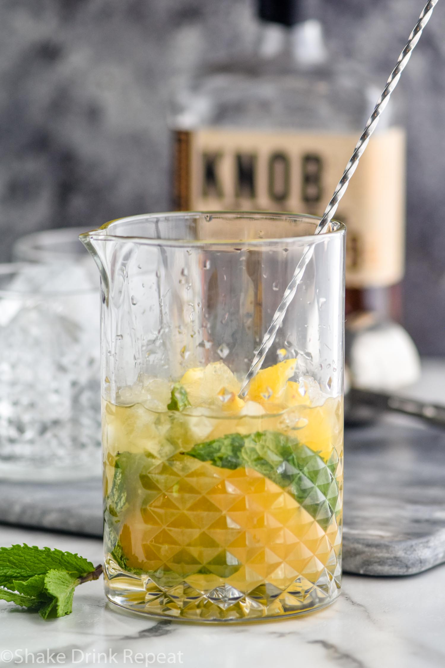 Making a whiskey smash by muddling mint and lemons in a mixing glass