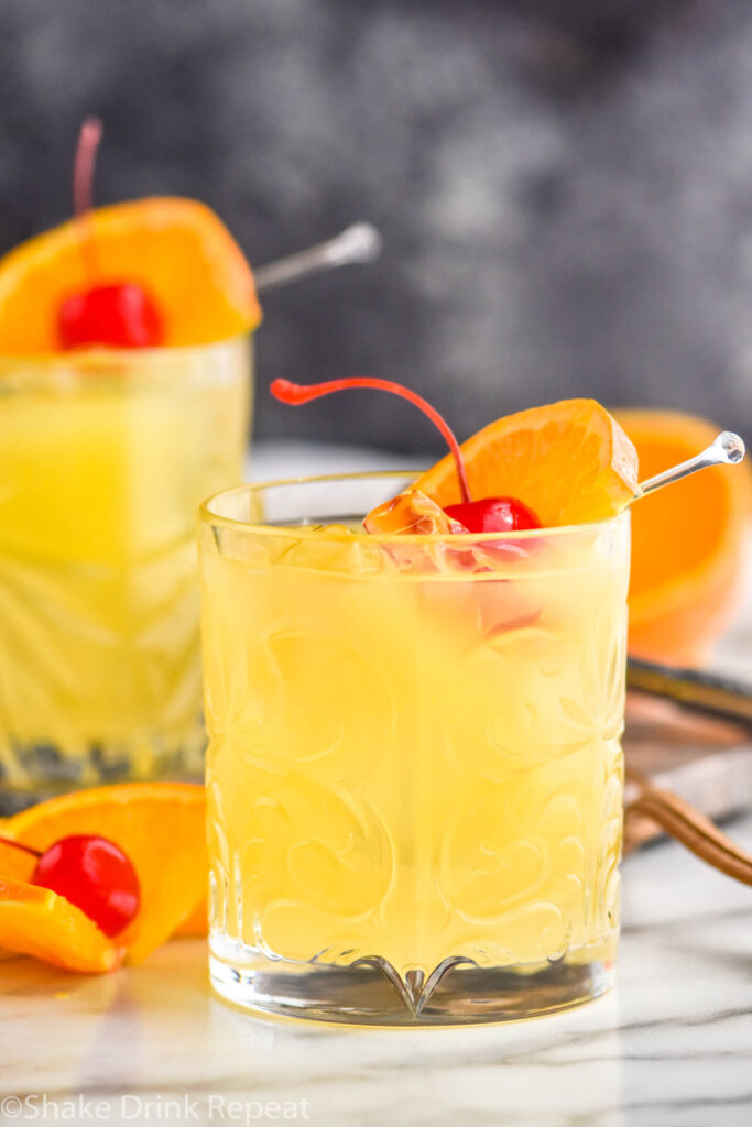 two glasses of Amaretto Stone Sour with ice, orange slice, and cherry garnish