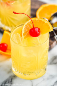 glass of Amaretto Stone Sour with ice, orange slice, and cherry garnish