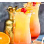 two glasses of bahama mama with ice, fresh orange slices, and cherry garnish surrounded by drink umbrella and straws