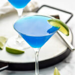 two martini glasses of blue daiquiri with fresh lime wedge garnish