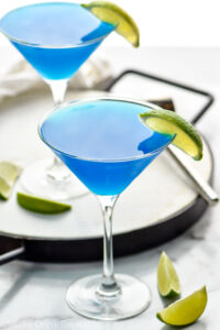 two martini glasses of blue daiquiri with fresh lime wedge garnish