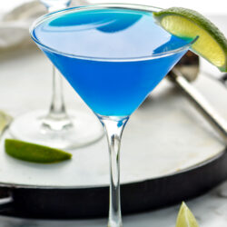 two martini glasses of blue Daiquiri with fresh lime wedges for garnish