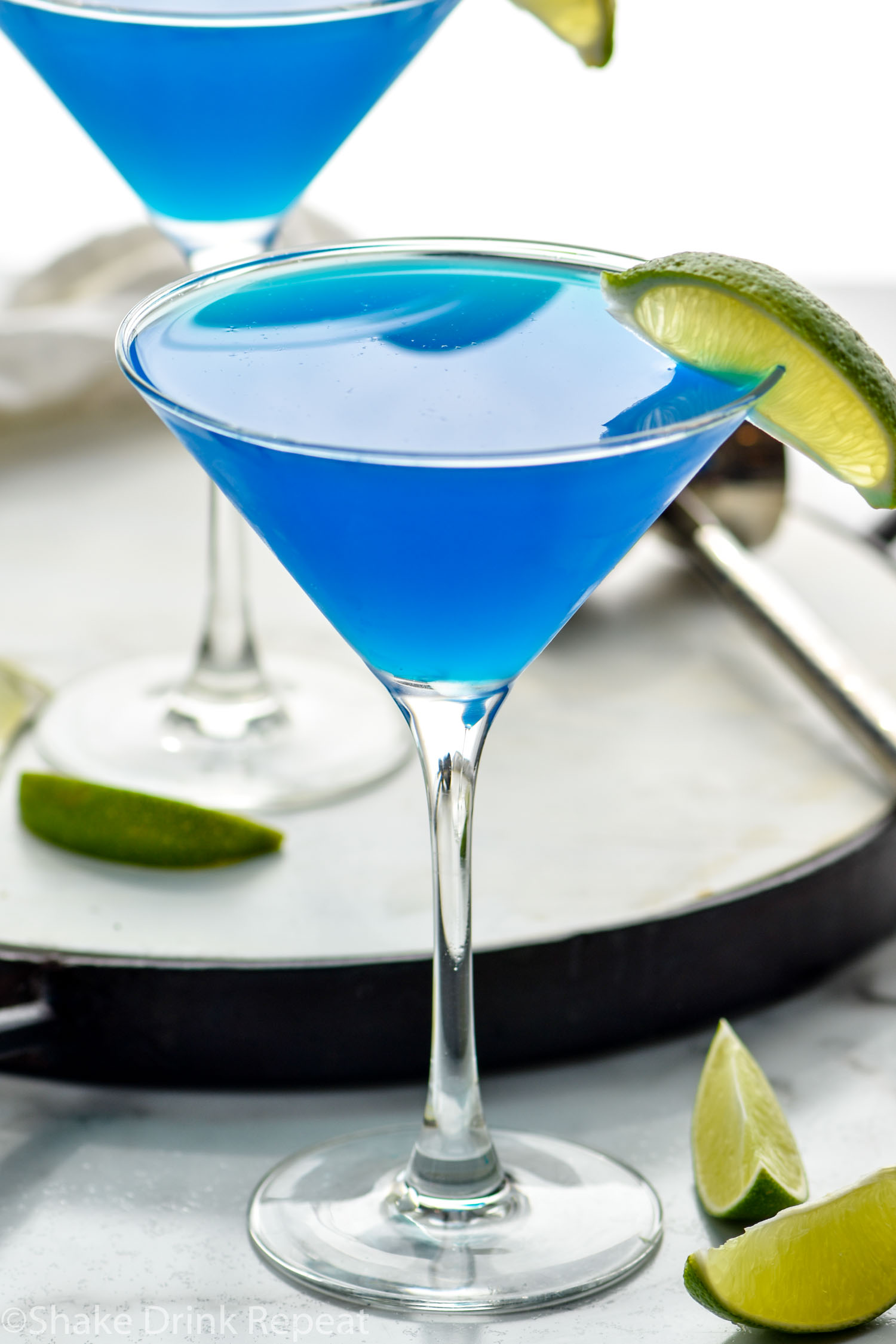 two martini glasses of blue Daiquiri with fresh lime wedges for garnish