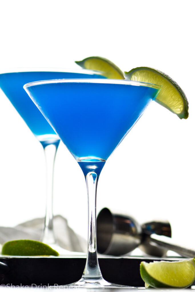 two martini glasses of blue daiquiri with fresh lime wedges