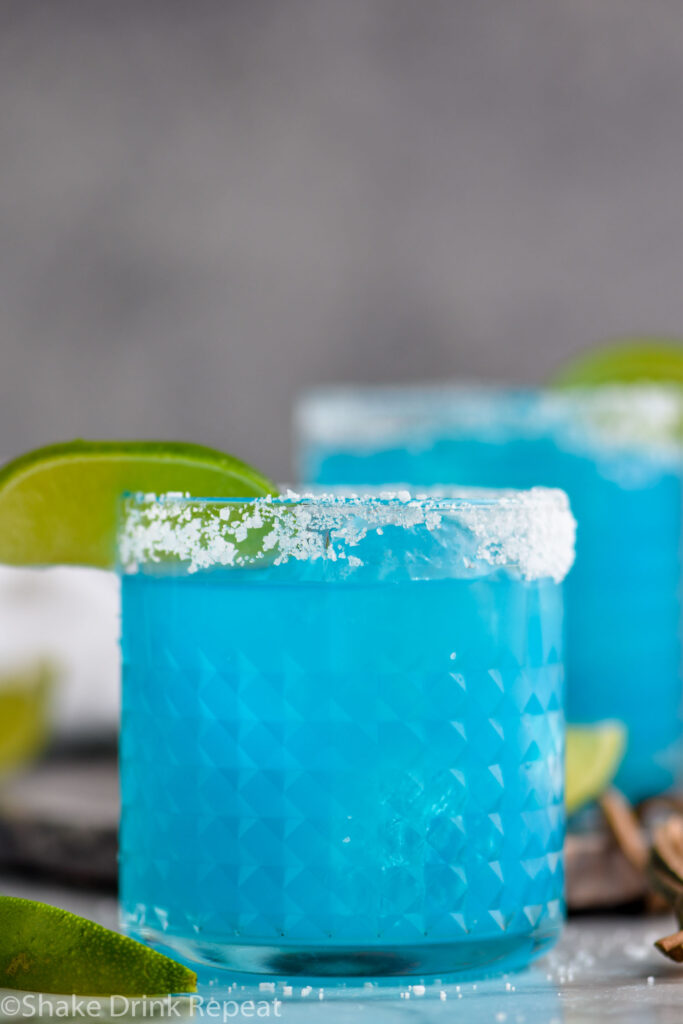 two glasses of blue margarita with salted rim and lime wedge garnish