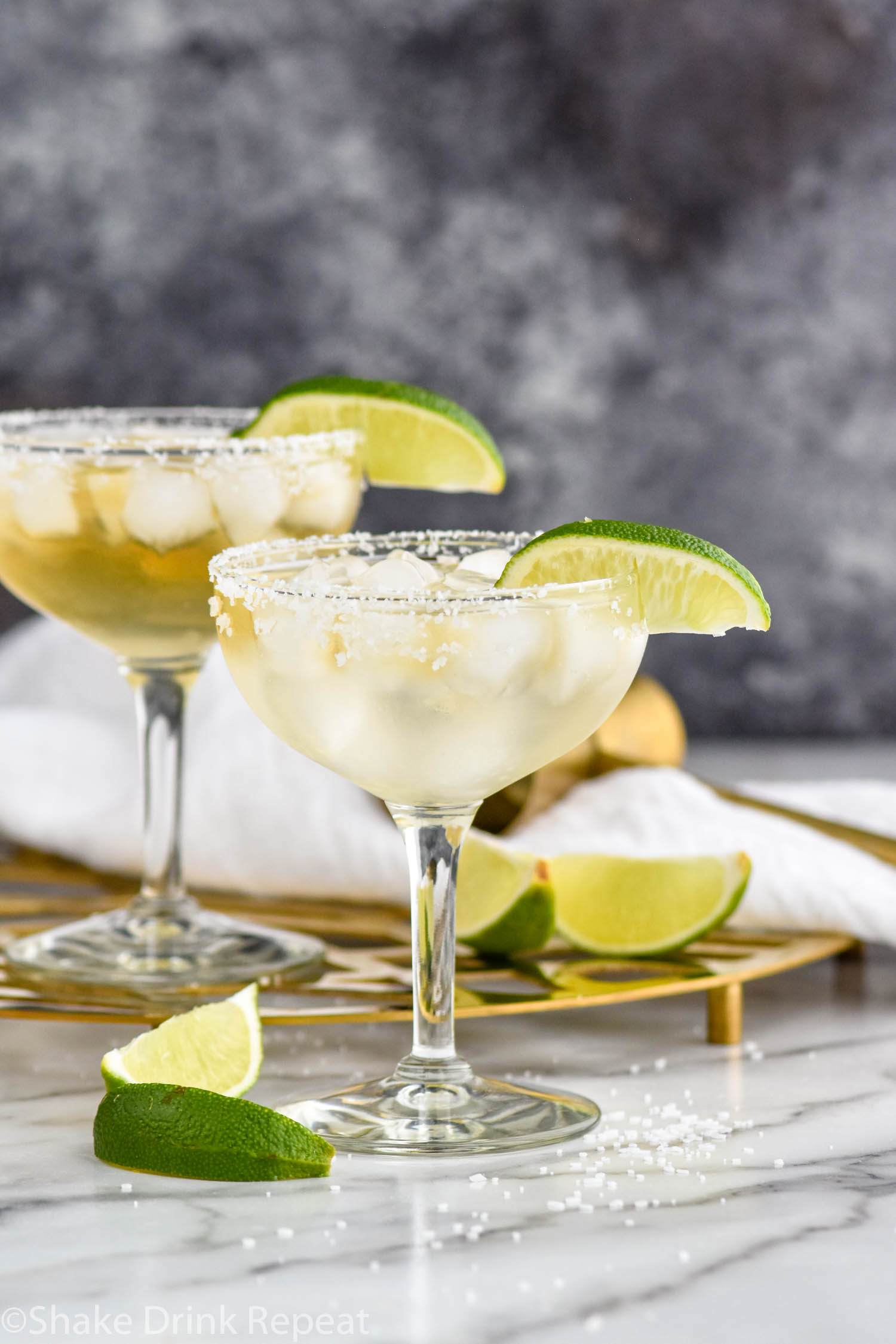 two glasses of Cadillac Margarita with salted rim, ice, and lime wedge garnish
