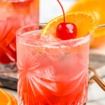 two glasses of cherry vodka sour with ice, orange slice and cherry garnish