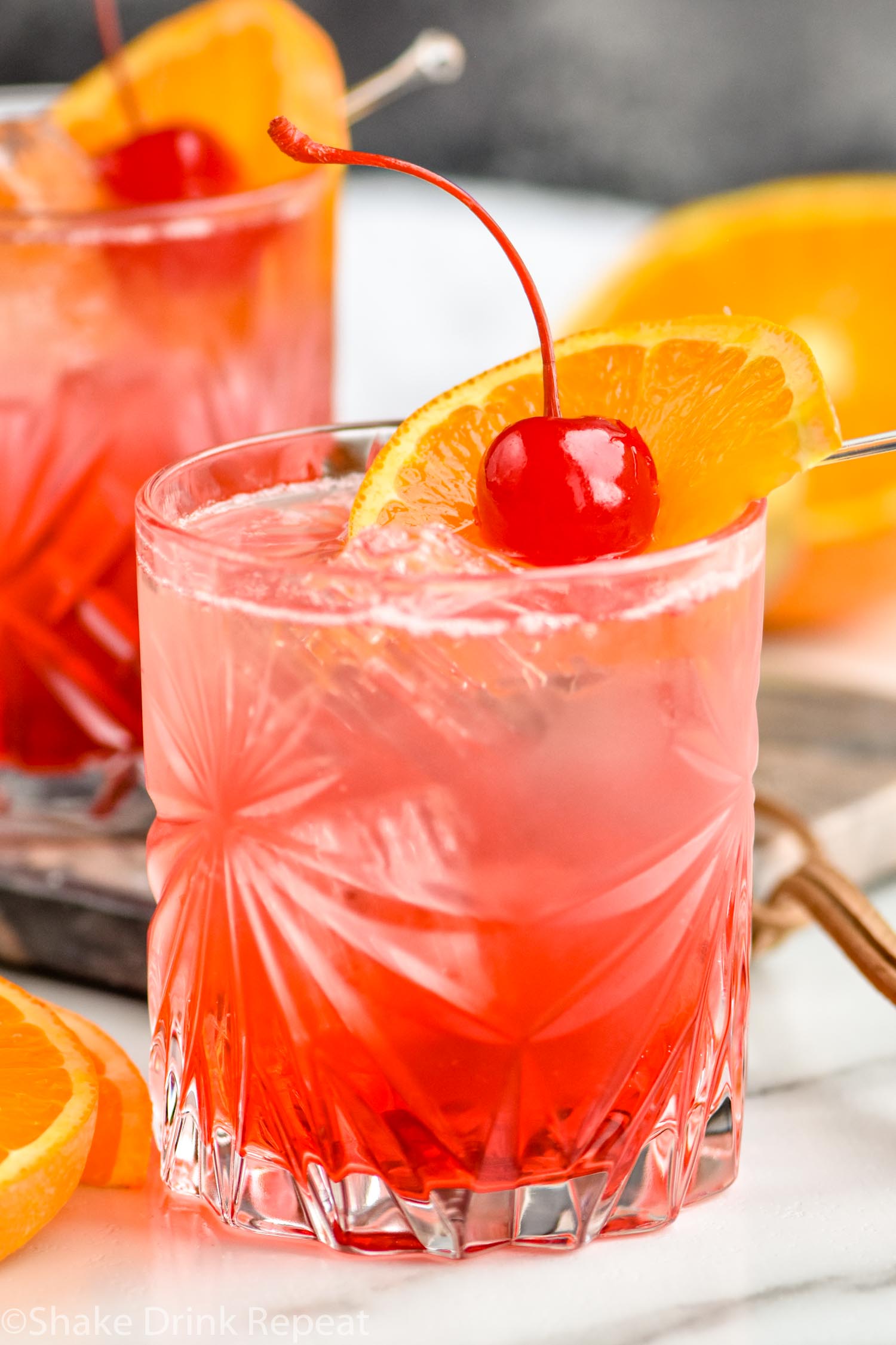 two glasses of cherry vodka sour with ice, orange slice and cherry garnish