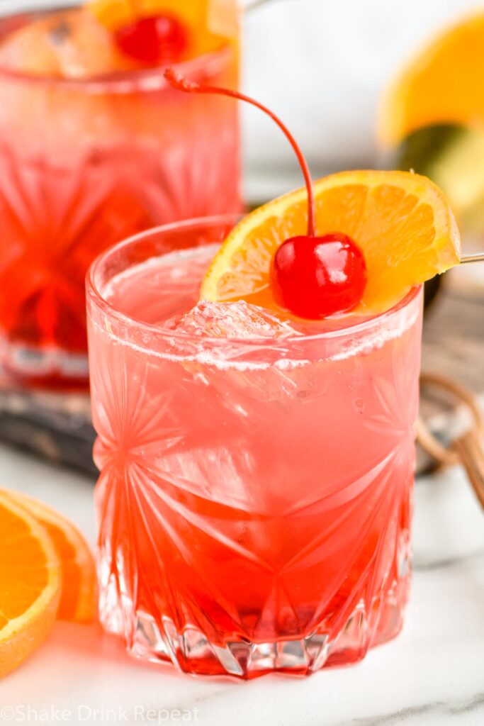 two glasses of cherry vodka soda with ice, orange slice and cherry garnish