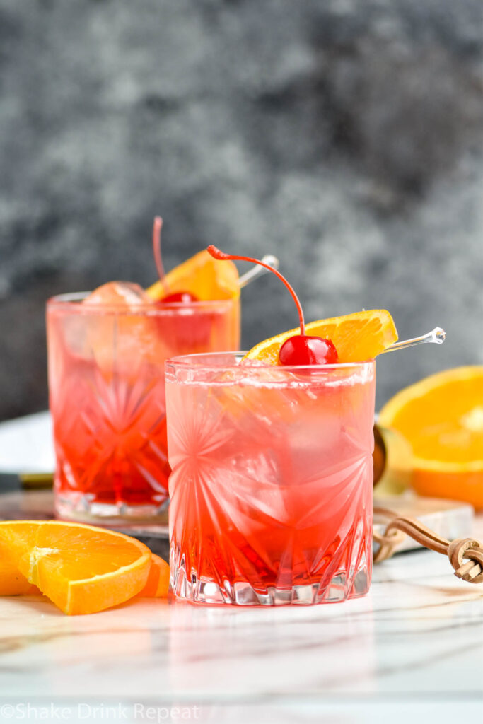 two glasses of Cherry Vodka Sour with ice and an orange slice and cherry garnish