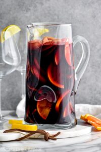pitcher of red sangria with slices of fresh fruit, lemons, and oranges