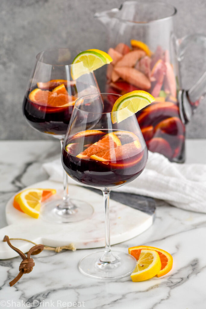 pitcher and two glasses of red sangria with fresh fruit including slices of lemons, limes, and oranges