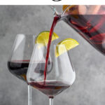 pouring red sangria from a pitcher into two wine glasses with slices of fresh lemons, limes, and oranges