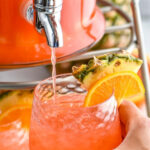 man holding a glass of ice filling with rum punch with fresh pineapple and orange