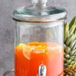 Glass dispenser of rum punch with ice and fresh fruit slices