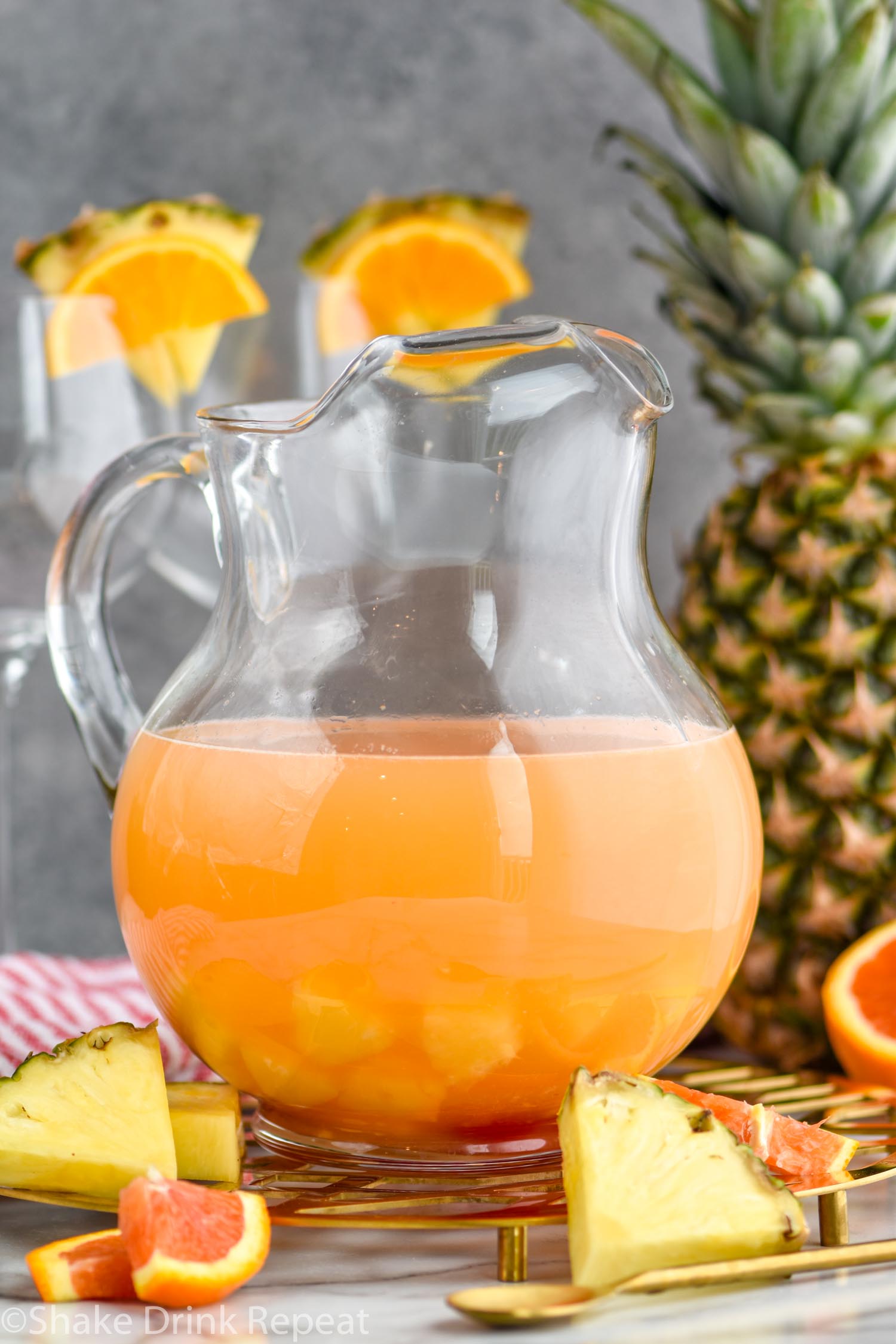 pitcher of tropical sangria surrounded by slices of fresh pineapple and oranges
