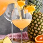 pitcher of tropical sangria pouring into glass garnished with slices of fresh pineapple and orange