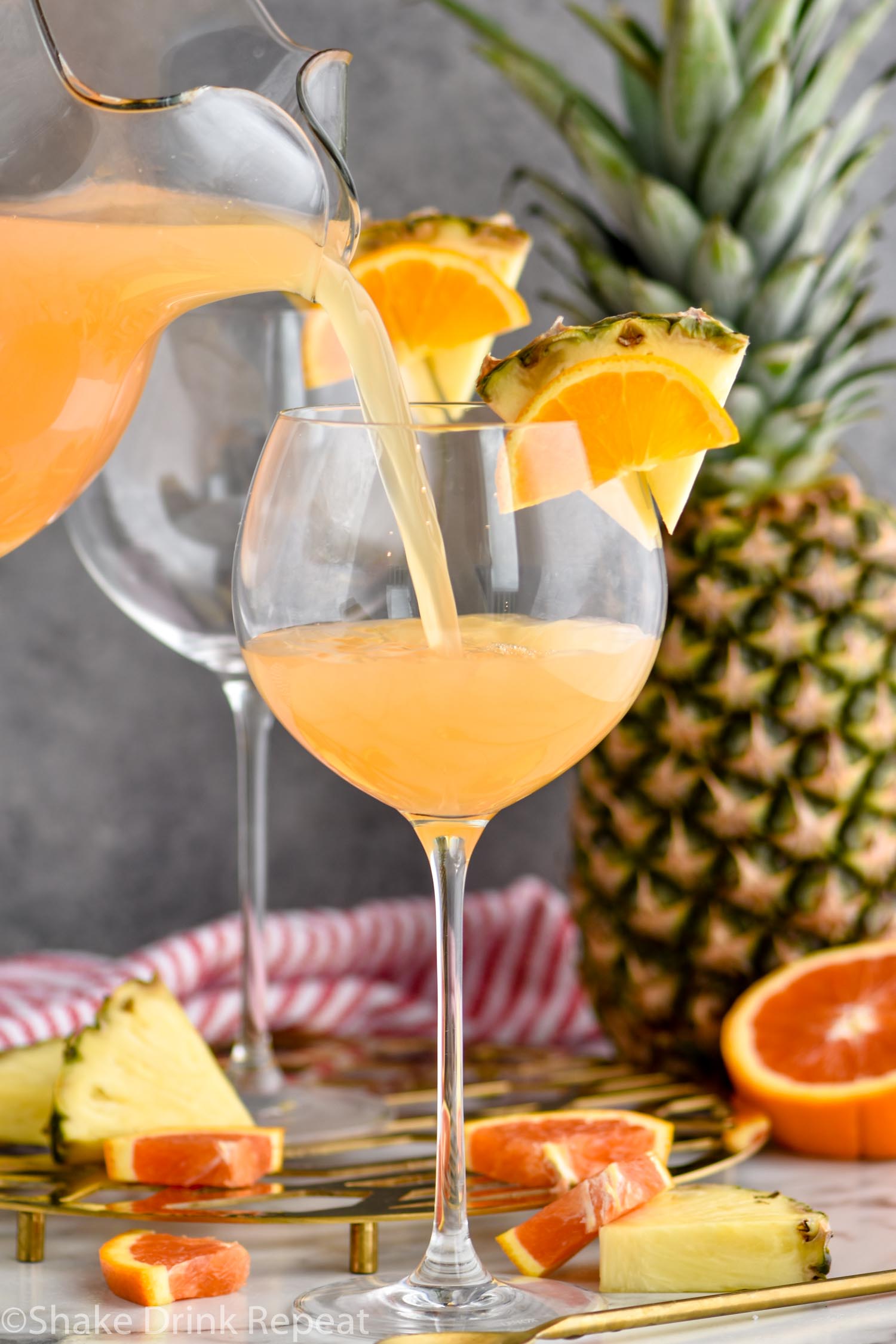 pitcher of tropical sangria pouring into glass garnished with slices of fresh pineapple and orange