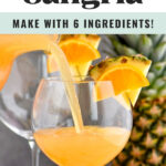 pouring tropical sangria into a glass garnished with slices of fresh pineapple and oranges