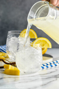 man pouring pitcher of lemonade into a glass of vodka and ice with lemon garnish