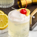 glass of vodka sour with fresh lemon slices and cherry garnish