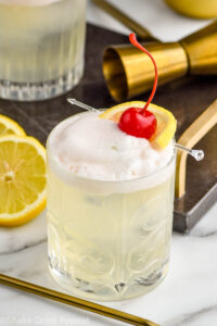 glass of vodka sour with fresh lemon slices and cherry garnish