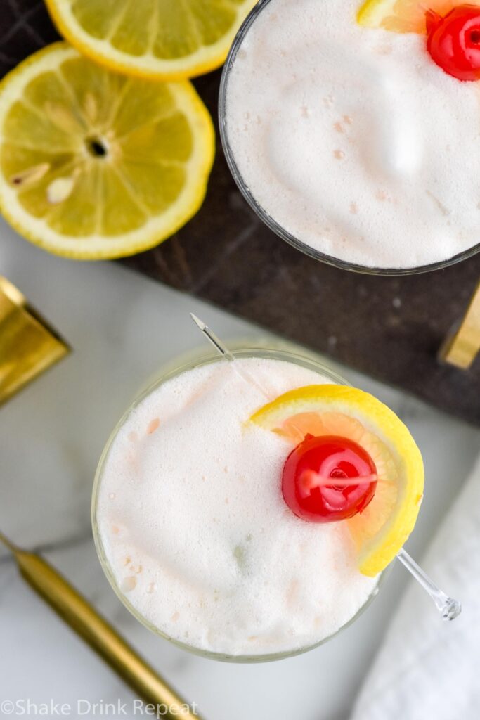 two glasses of vodka sour with frothy egg white, fresh lemon slices, and cherry garnish