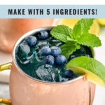 two copper mugs of blue mules with ice, blueberries, lime wedge, and mint leaves