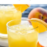two glasses of Fuzzy Navel cocktail with ice and orange slice garnish surrounded by fresh peach slices and two straws