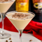 two martini glasses of Mudslide recipe surrounded by chocolate shavings, two straws, a bottle of Bailey's and a bottle of Kahlua