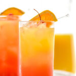 two glasses of tequila sunrise with ice, orange slice and cherry garnish