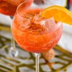 glass of Aperol Spritz with ice, fresh orange slice garnish with bottle of sparkling wine in the background