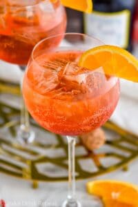 glass of Aperol Spritz with ice, fresh orange slice garnish with bottle of sparkling wine in the background