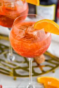 glass of Aperol Spritz with ice, fresh orange slice garnish with bottle of sparkling wine in the background