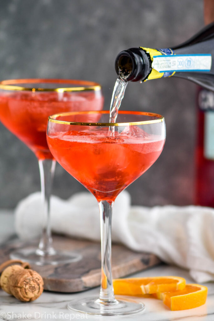 bottle of prosecco pouring into a glass of Campari Spritz with ice and orange slices