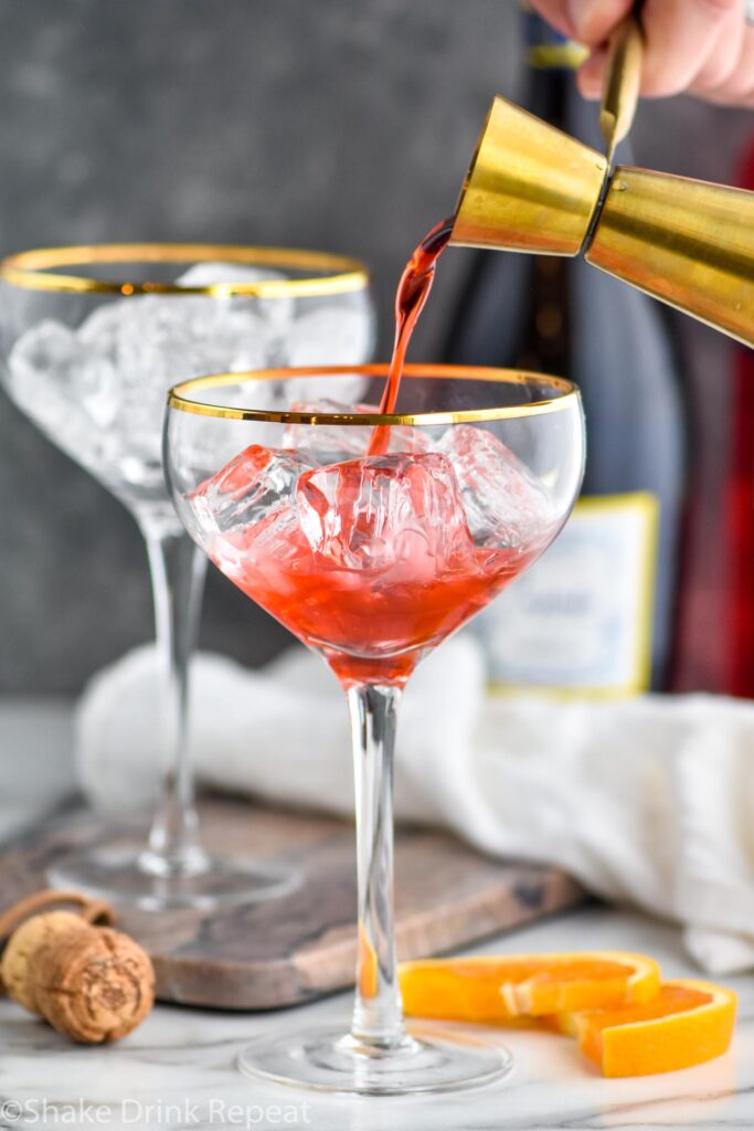 jigger of Campari pouring into a glass of ice to make a Campari Spritz