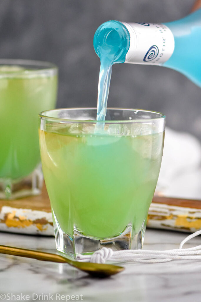 pouring bottle of Hptoniq into a glass of incredible hulk ingredients with ice and gold spoon