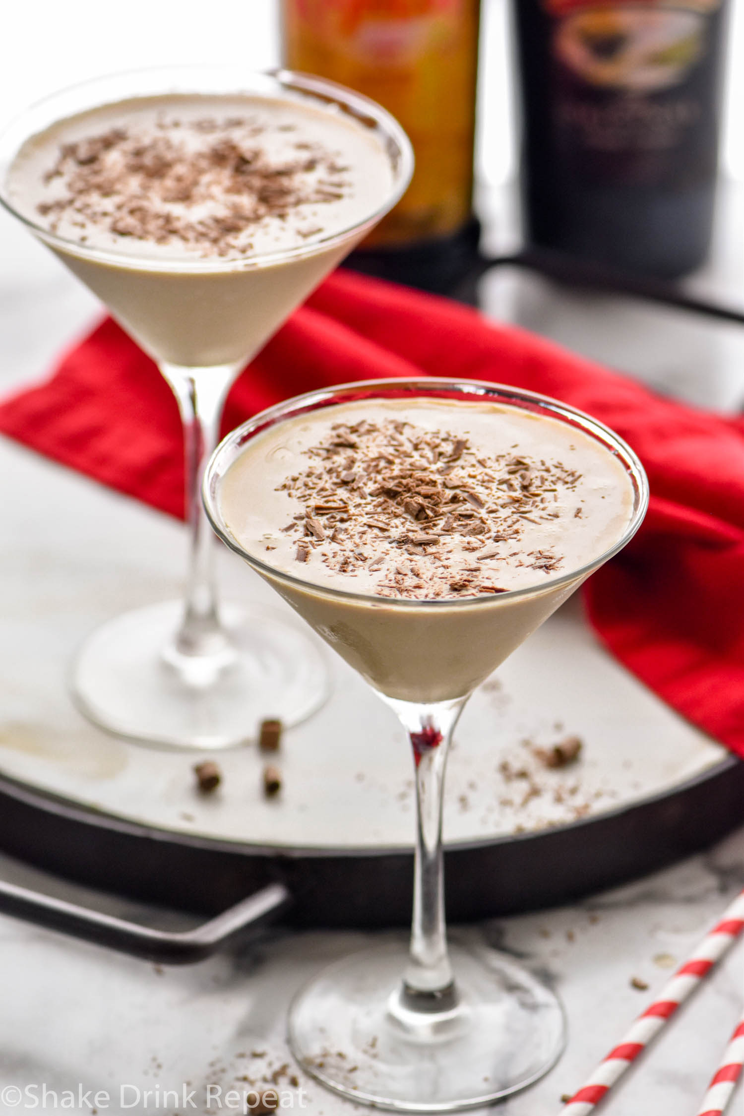 two martini glasses of Mudslide recipe surrounded by chocolate shavings, two straws, a bottle of Bailey's and a bottle of Kahlua