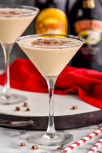 two martini glasses of Mudslide recipe surrounded by chocolate shavings, two straws, a bottle of Bailey's and a bottle of Kahlua