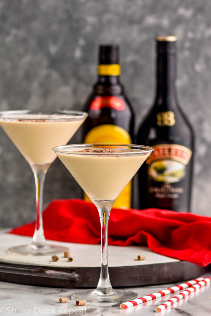 two martini glasses of Mudslide recipe surrounded by chocolate shavings, two straws, a bottle of Bailey's and a bottle of Kahlua