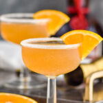 two glasses of Sidecar cocktail with sugared rim, fresh orange slice garnish and bottle of Cognac in the background