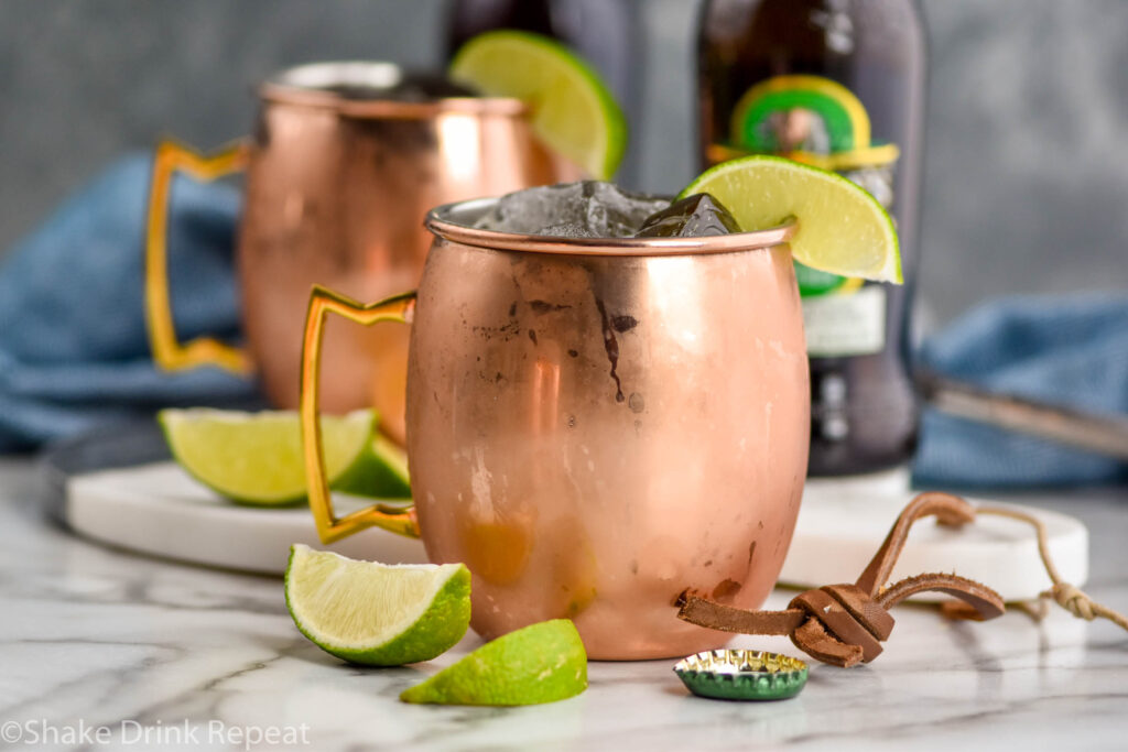 two copper mugs of tequila mules with ice, fresh lime wedges, and bottles of ginger beer