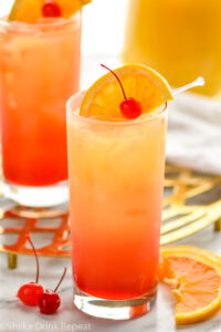two glasses of tequila sunrise with ice and orange slice and cherry garnish