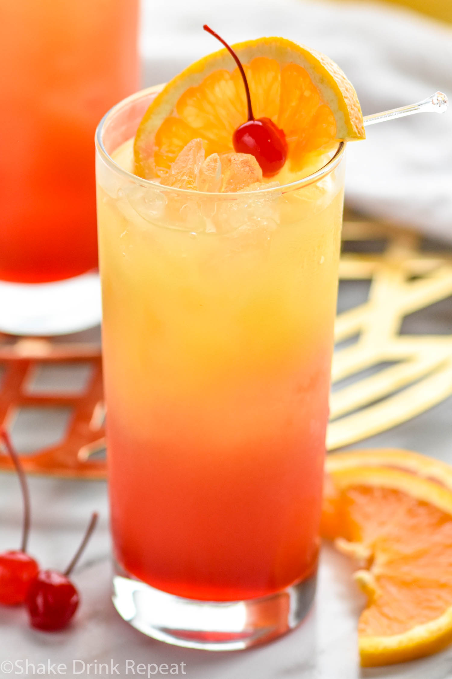 glass of tequila sunrise with ice and an orange slice and cherry garnish