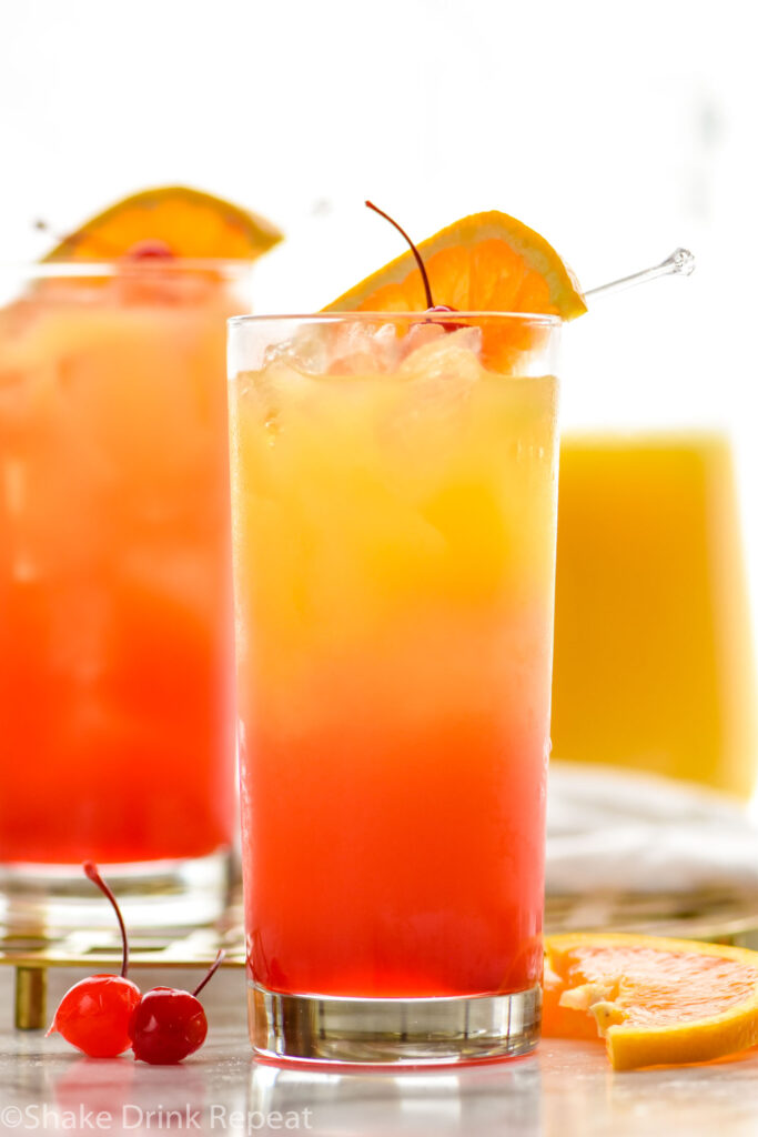 two glasses of tequila sunrise with ice and fresh orange slice and cherry garnish