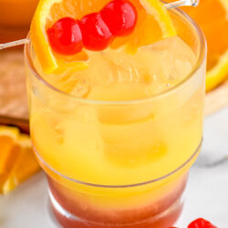 glass of tequila sunset with ice and cherries and orange slice as garnish