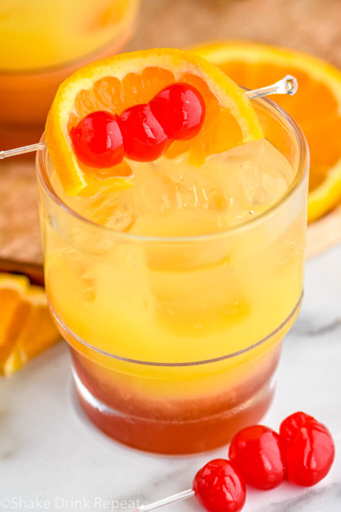 glass of tequila sunset with ice and cherries and orange slice as garnish