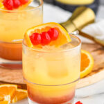 two glasses of tequila sunset with ice and cherries and orange slice garnish with bottle of blackberry brandy in the background
